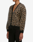 A person wears the FRAME Brushed Leopard Cardi, a fuzzy leopard-print cardigan with black trim on the cuffs and hem, paired with black pants, against a plain white background.