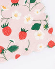 Faire Strawberry Napkins feature a scalloped edge and are adorned with red strawberries, green leaves, and white strawberry flowers, displayed on a pink background.