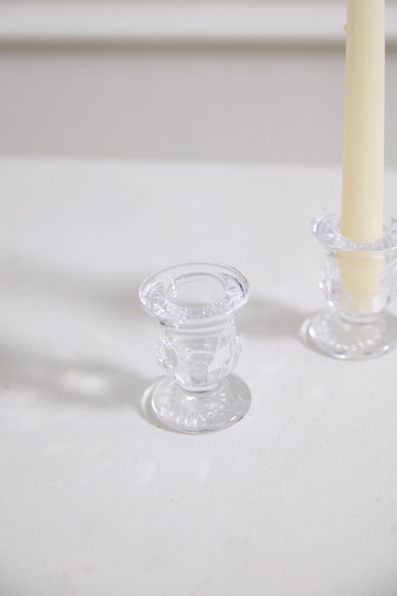 The Bellamy Candleholder by Accent Decor, in clear glass and urn-shaped, sits on a white surface beside its matching taper holder with a pale yellow candle.