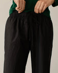 A person in a green top adjusts the drawstring of The Pop Pant, made from 100% cotton poplin by Donni, against a neutral background.