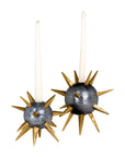 Two white tapered candles sit in Punk Candleholders by The Import Collection, featuring round gold bases with metallic spikes reminiscent of starbursts or sea urchins, creating a bold industrial accent against a white background.