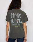 A person with long, curly hair is wearing an organic cotton People Of Leisure tee featuring a faded "Pink Floyd North American Tour" design. They're standing with their back to the camera, showcasing the iconic artwork and timeless style.