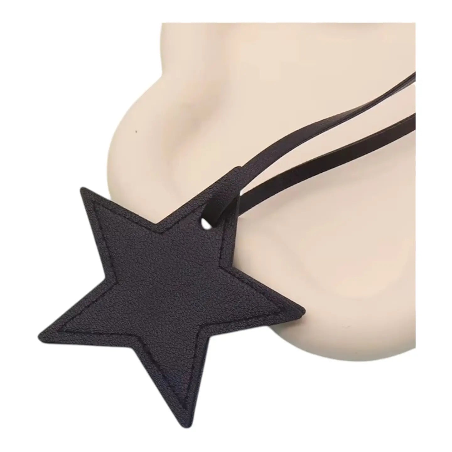 The Faire Bag Charm is a black leather, star-shaped accessory with a matching strap—ideal as a personal touch or chic handbag accent—displayed on a smooth cream surface.