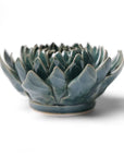 The Dahlia Teal by Chive Ceramics (thru Faire) is a handmade ceramic bowl with glossy blue-green, dahlia-shaped petals, ideal for lovers of unique pottery and ceramic flowers, shown on a plain white background.