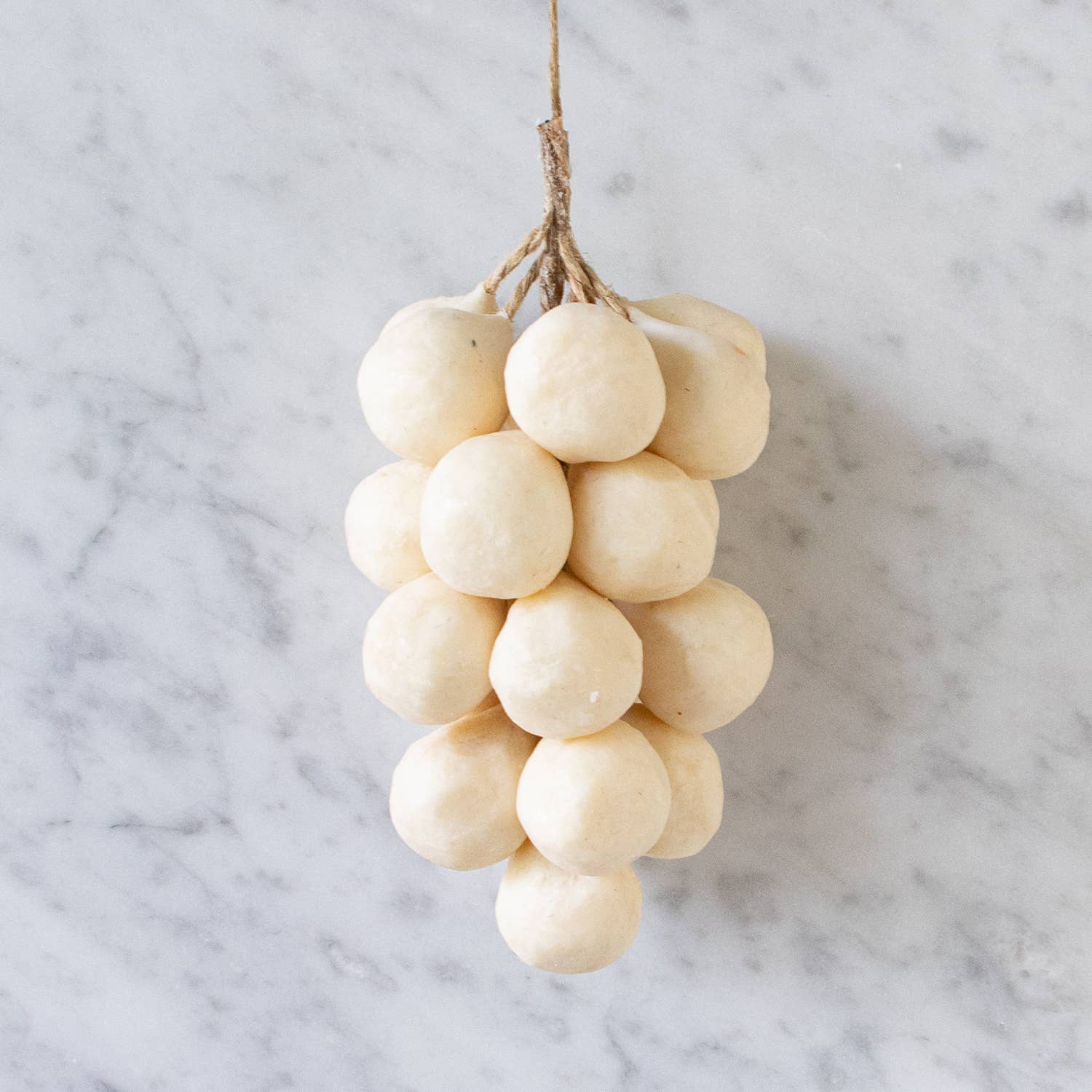 Faire’s Handcrafted Grapes Soap features round, pale white soaps shaped like a grape cluster and tied with twine, displayed on a light marble surface.