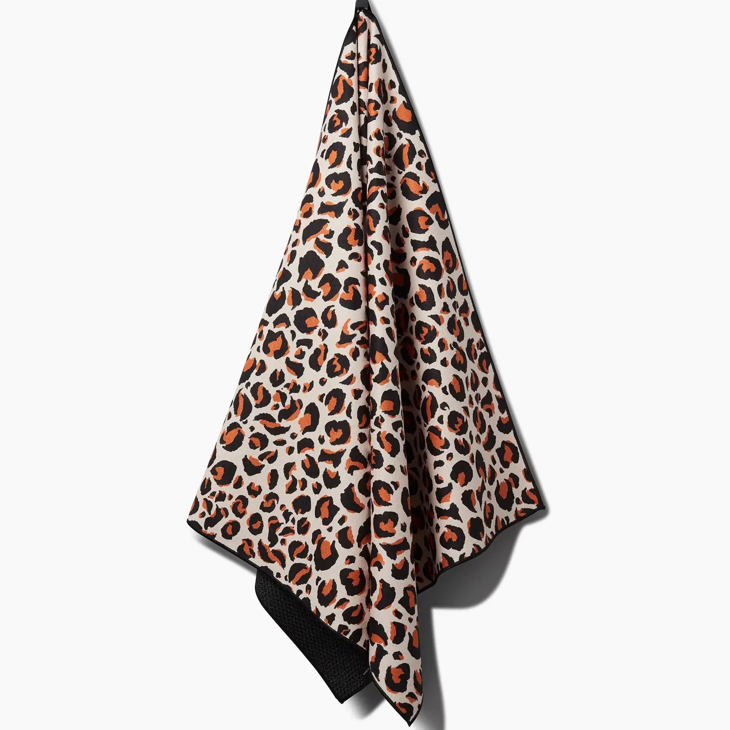 The Faire Leopard Yoga Towel features a bold orange, black, and beige leopard print and ultra-absorbent fabric, shown hanging from a hook against a white background.
