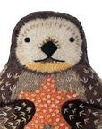 The Otter Embroidery Kit by Faire lets you create a plush otter holding an orange starfish, featuring detailed embroidered stitching, all set against a white background.