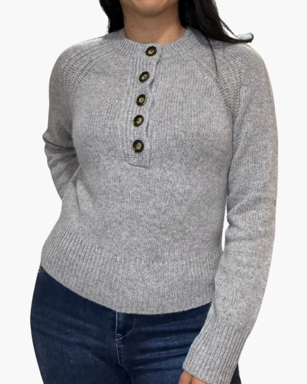 A person wears the White + Warren Cashmere Luxe Henley in light gray, featuring five dark front buttons, paired with dark blue jeans. The background is plain white.