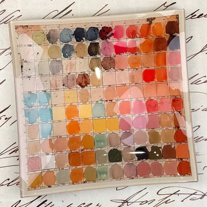 The Faire Watercolor Artist's Palette Glass Tray features a grid of vibrant watercolor swatches—blues, pinks, reds, oranges, yellows, and browns—overlaid on paper with elegant cursive script for an inspiring artful accent.