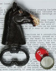 The HomArt Horse Head Bottle Opener, hand-painted, sits on a typed page with a removed bottle cap and a red "Cola" cap nearby.