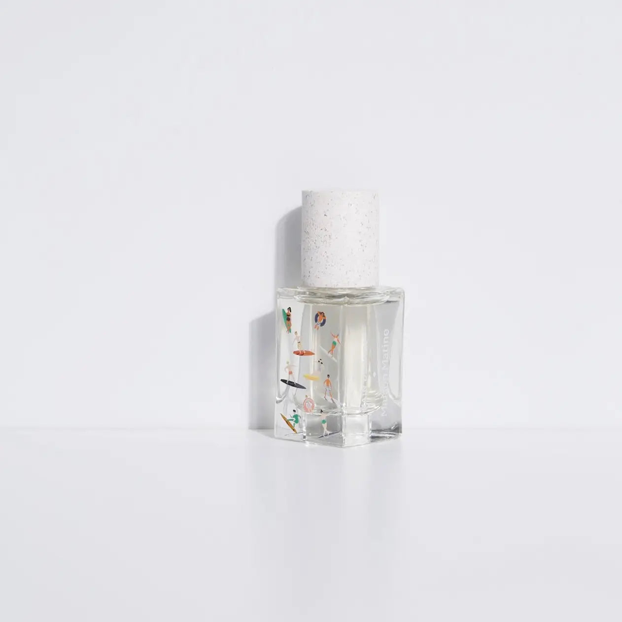 The Maison Matine Perfume by Faire features a clear glass bottle with a white speckled cap, filled with transparent liquid and small colorful accents, evoking bergamot and musk notes against a plain white background.