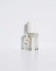 The Maison Matine Perfume by Faire features a clear glass bottle with a white speckled cap, filled with transparent liquid and small colorful accents, evoking bergamot and musk notes against a plain white background.
