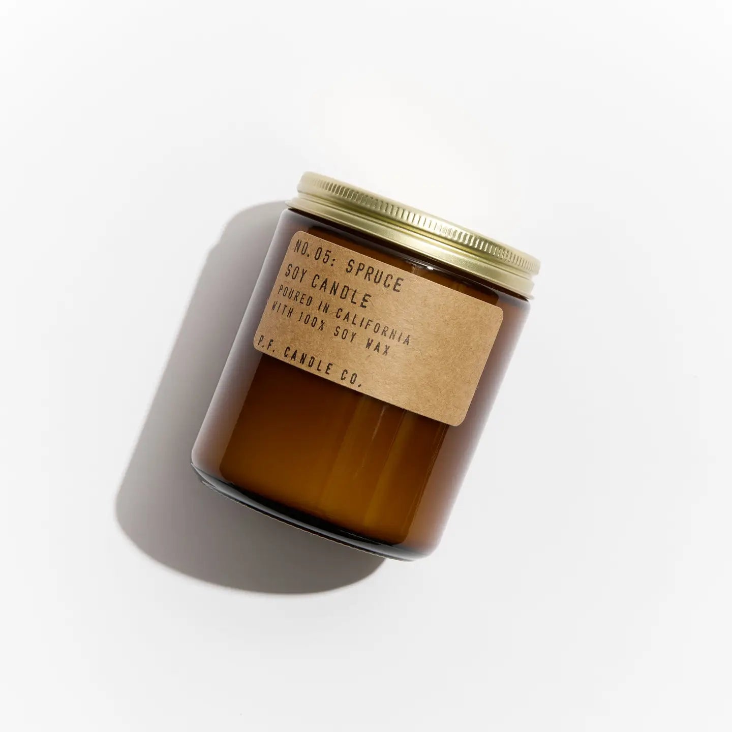 A brown glass jar candle with a gold metal lid and kraft label reading “PFC Candle” by Faire sits on a white background—one of their hand-poured candles, crafted with fine fragrance oils for an inviting aroma.