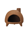 A terra-cotta-colored clay outdoor pizza oven features a domed shape with an open front and rests on three short legs for stability. It is topped with Creative Co-op's Footed Incense Chimney on the top right.