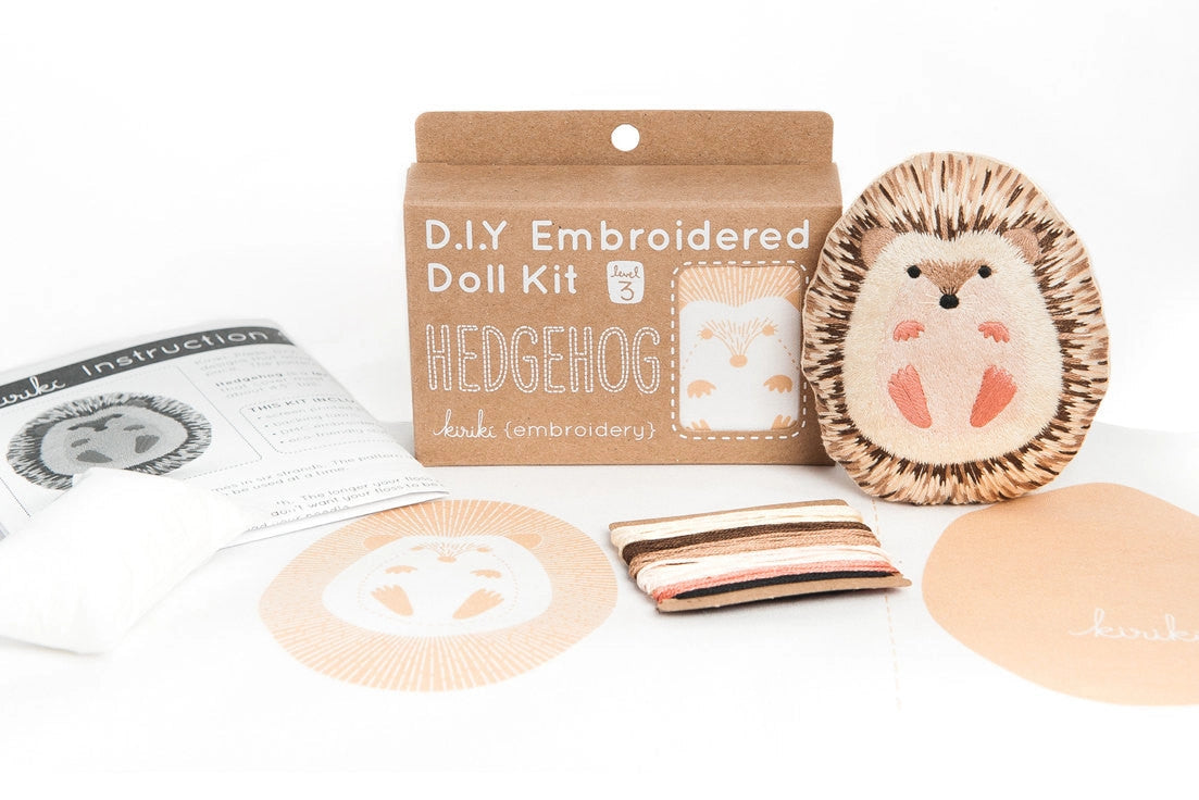 The Faire Hedgehog Embroidery Kit includes a hedgehog pattern, finished doll, instructions, fabric pieces, colorful thread, and a Level 3 "Hedgehog" box—perfect for anyone who loves making embroidered dolls.