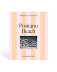 The Faire Pieceworks Puzzle 1000 features pink and peach stripes, "Positano Beach" text, and a small photo of colorful umbrellas on a packed Positano beach—evoking Slim Aarons’ iconic, midcentury seaside style.