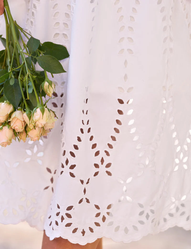 A person in the Frank & Eileen Gracie Midi Eyelet Dress with intricate cut-out embroidery along the hem holds a small bouquet of pale peach roses.