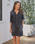 Frank & Eileen Ireland Utility Dress with rolled sleeves, styled outdoors by white flowers on a wooden deck.