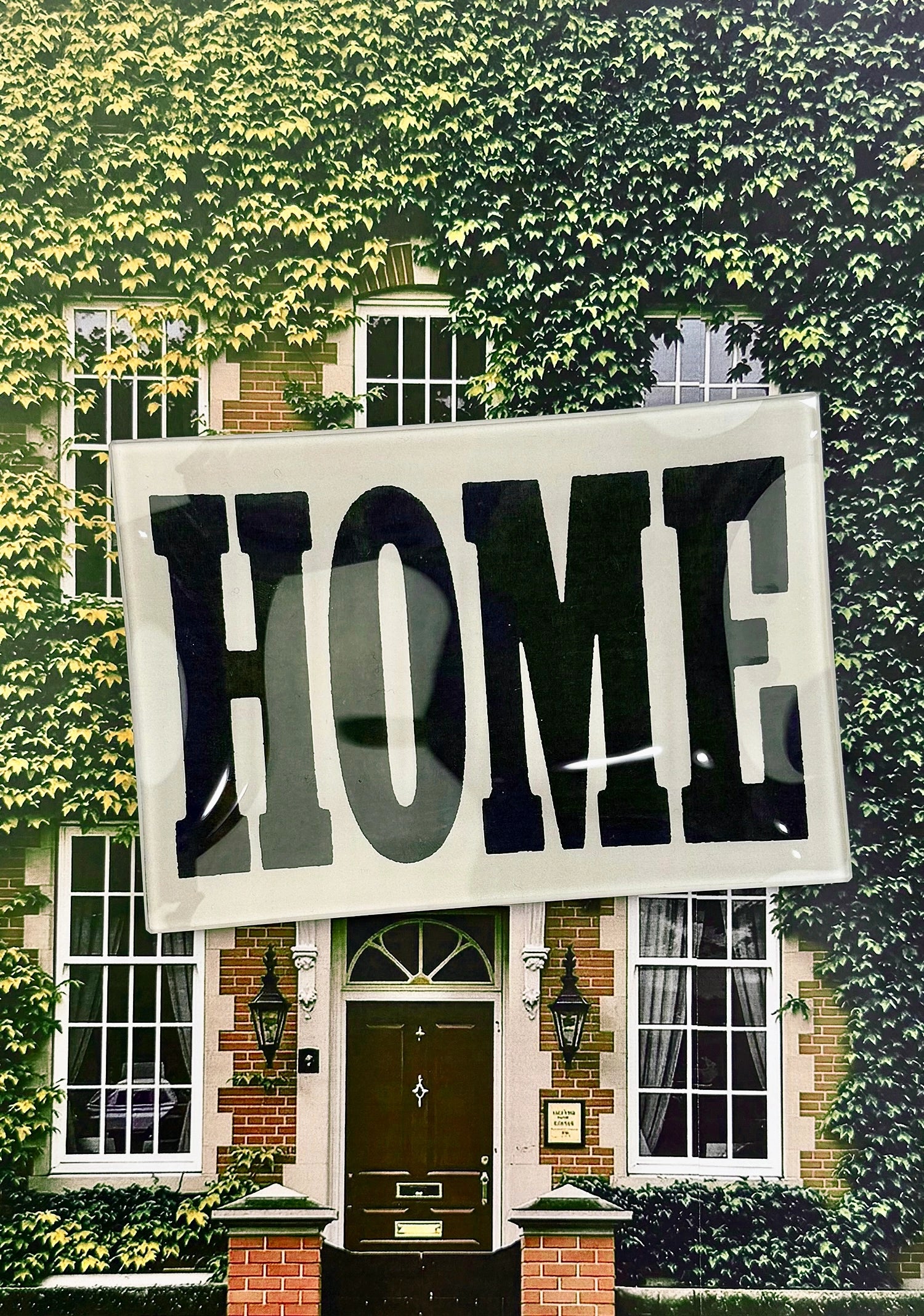 The Faire Home Block Glass Tray features vintage "HOME" typography in bold black, perfect for displaying against house exteriors with green ivy, brickwork, large windows, and a central dark door.