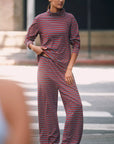 A person stands on a city street wearing Donni's The Striped Jersey Turtleneck with matching wide-leg pants and sandals, gazing calmly to the side.