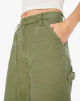 A person wears The Half Chisel high-waisted cargo pants by Mother in army green, featuring utility patch pockets and detailed stitching, paired with a white ribbed crop top. One hand rests in the pocket, highlighting the pants’ design.
