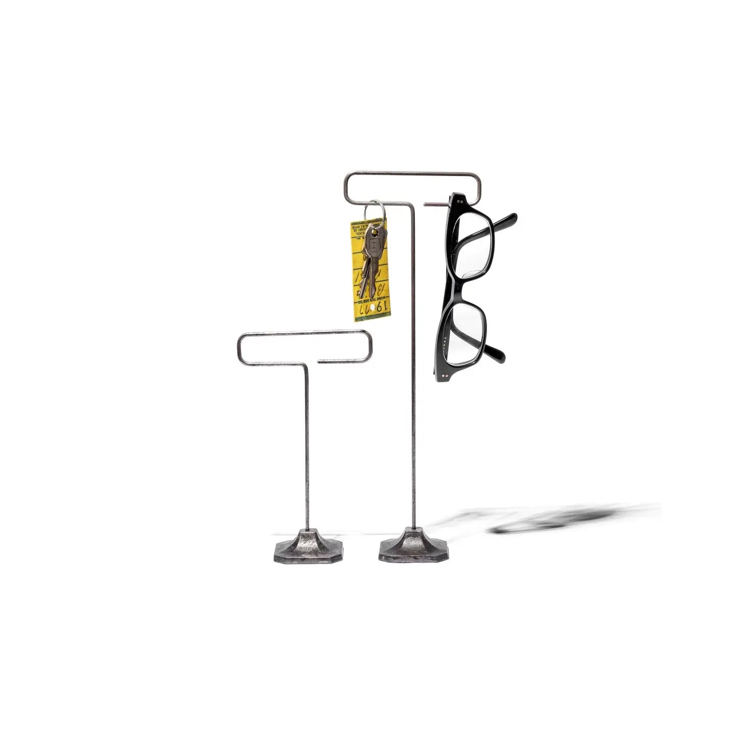 Two Faire Desk Wire Display Stand S units with a minimalist design are shown against a plain white background: the taller displays black eyeglasses and yellow-tagged keys, while the shorter stand remains empty.