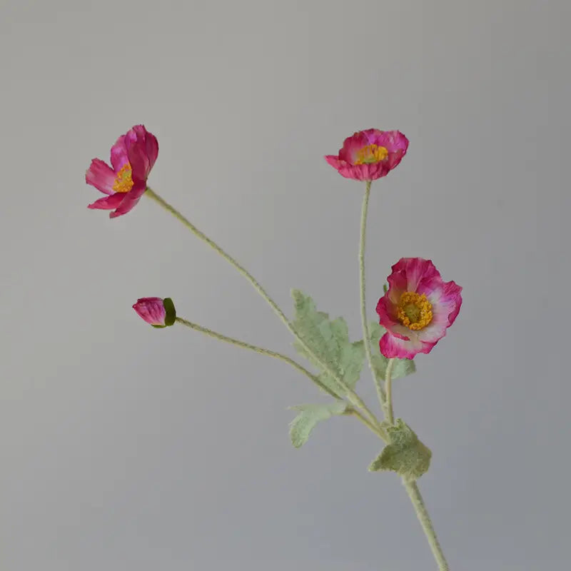 The Faire 22'' Single Flocked Floral Poppy Spray features four pink silk blossoms and green leaves on an elegant stem, beautifully displayed against a plain, light gray background.