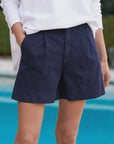 A person in a white long-sleeve top and Waterford Shorts by Frank & Eileen stands by the swimming pool, hands casually in pockets, against a softly blurred background.