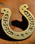 The Faire Good Luck Pin is a brass enamel pin engraved with “GOOD LUCK” and stars, shown resting on a wooden surface.