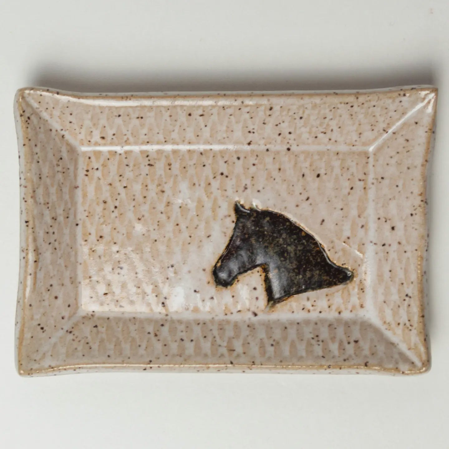 The Horse Trinket Tray by Faire is a rectangular, speckled stoneware tray with a textured finish, showcasing a black horse head silhouette on a light creamy beige background for a rustic and artistic look.