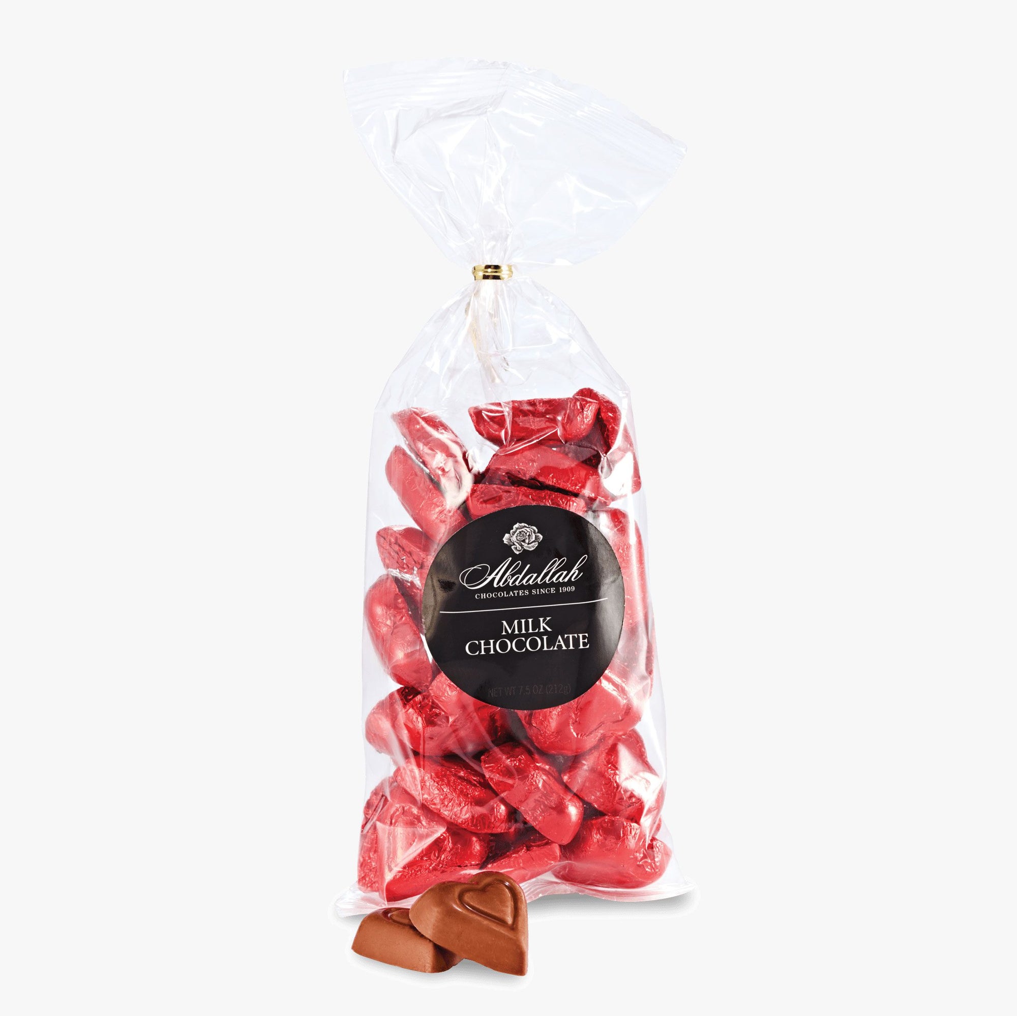 A clear plastic bag from Abdallah, labeled "Milk Chocolate" in silver on black, contains heart-shaped milk chocolates wrapped in shiny red foil. Two unwrapped chocolates are displayed invitingly in front of the bag.