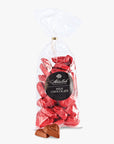 A clear plastic bag from Abdallah, labeled "Milk Chocolate" in silver on black, contains heart-shaped milk chocolates wrapped in shiny red foil. Two unwrapped chocolates are displayed invitingly in front of the bag.