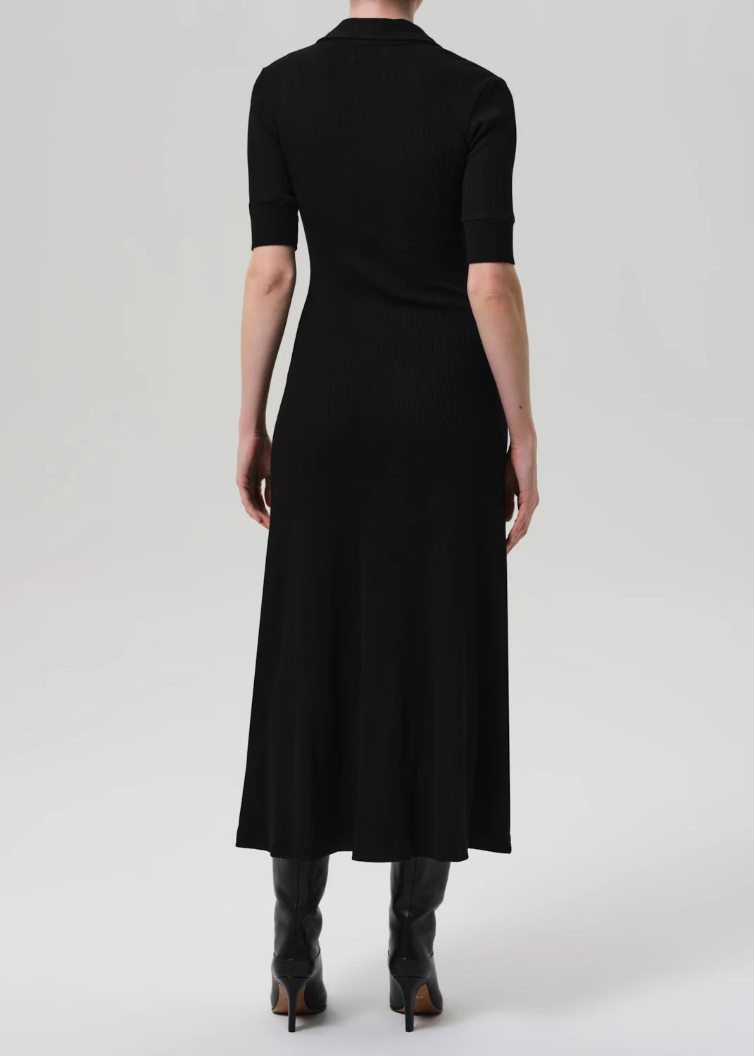 A person wearing the Citizens Of Humanity/AGOLDE Amina Polo Dress with black knee-high boots stands facing away from the camera against a plain, light background.