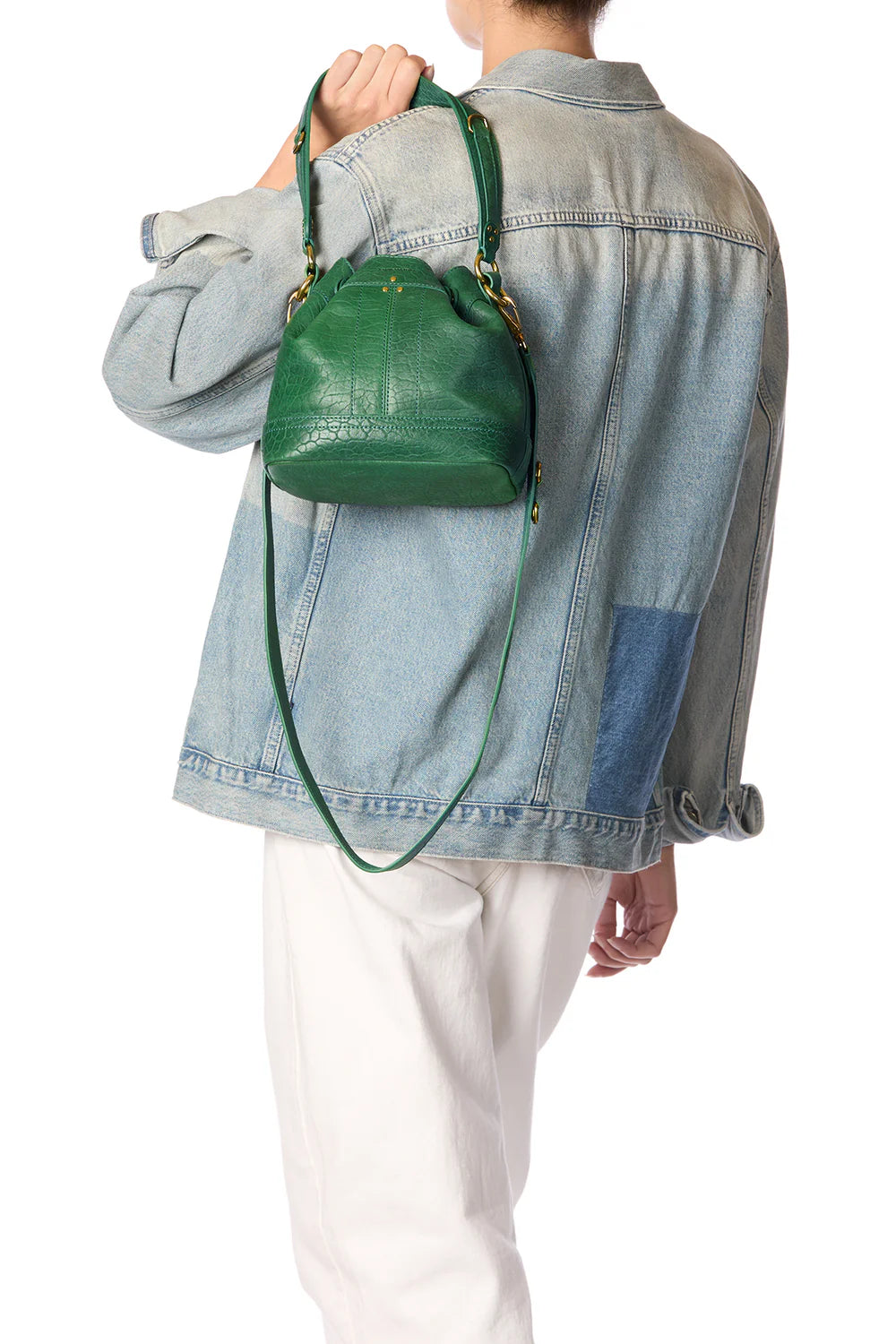 A person in a denim jacket and white pants carries the Jerome Dreyfuss &quot;Ben Small Bucket,&quot; a green leather bag with a shoulder strap. The look is casual, and their face isn&#39;t visible.