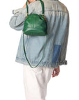 A person in a denim jacket and white pants carries the Jerome Dreyfuss "Ben Small Bucket," a green leather bag with a shoulder strap. The look is casual, and their face isn't visible.