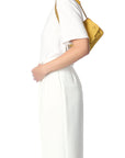 Against a white background, a person in a white outfit is holding the Lulu Small Bag by Jerome Dreyfuss, a yellow mini messenger bag with a leather strap over their shoulder.