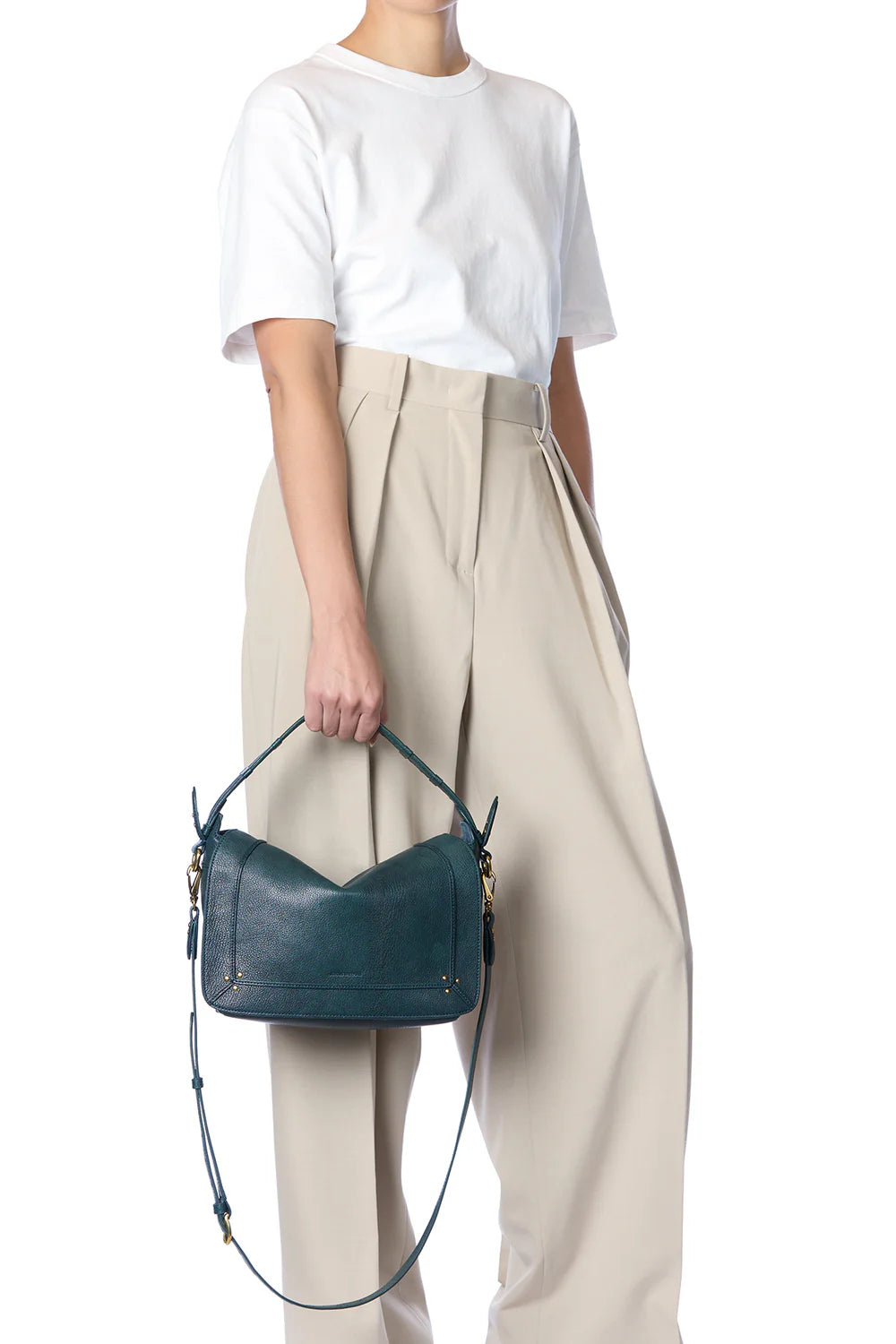 A person in a white t-shirt and beige wide-leg pants holds the Jerome Dreyfuss Pepito Medium Bag, featuring a quilted leather handle and adjustable strap. The image highlights the outfit and handbag against a plain white background.