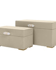 The Import Collection’s Ramato Box set features two beige rectangular fabric storage boxes in different sizes, each with gold-accented crystal handles and small gold feet—a chic accent for modern home decor.