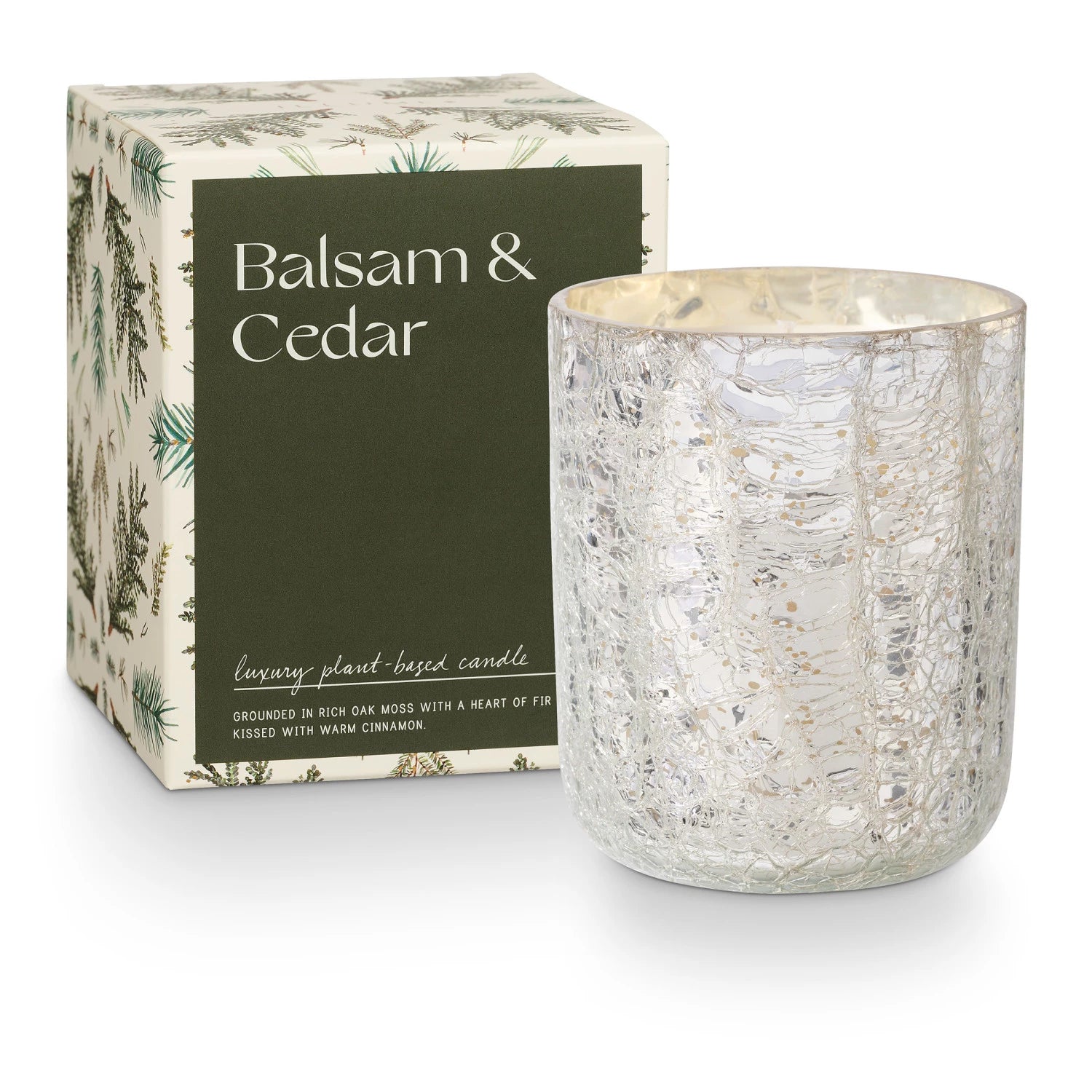 A Crackle Glass Candle Small by Creative Co-op is housed in a decorative, silver-textured holder beside a compact green and white box labeled "Balsam & Cedar," showcasing an elegant botanical design.