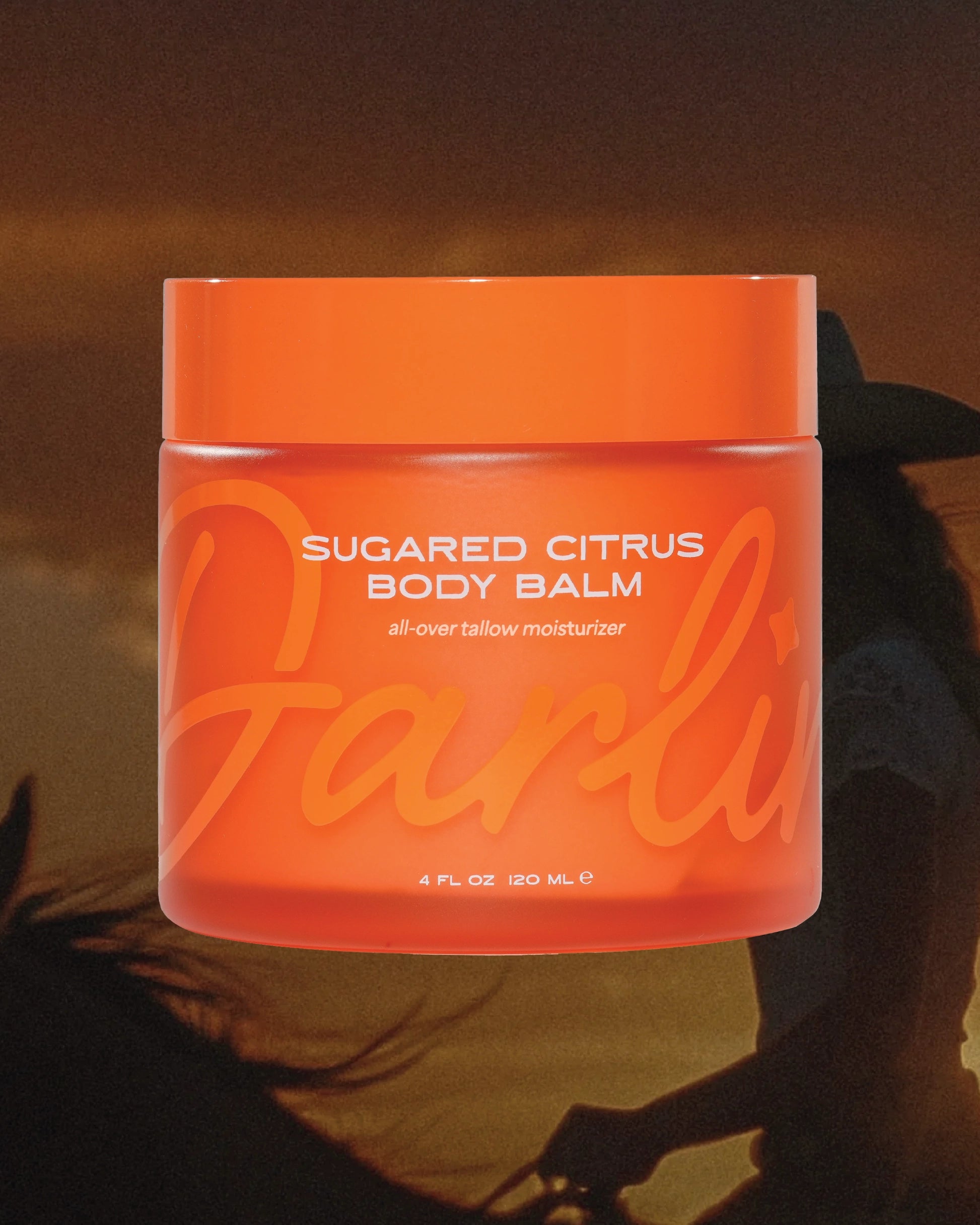 An orange jar labeled "Tallow Body Butter Moisturizer" by Faire, 4 fl oz (120 mL), made with grass-fed beef tallow and Sarasota honey, is shown before a silhouette of a person on horseback at sunset.