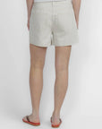 A person stands with their back to the camera, wearing FRAME’s The Off Duty Long Hang Short in light beige and brown sandals with orange soles, set against a plain white background.