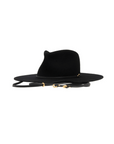 The Maxine Black Fedora by Ninakuru is a black wool hat with a wide brim and high crown, featuring a thin vegetable-tanned leather chin strap adorned with gold accents. It's ideal for sun protection, and its elegance shines through against the plain white background.