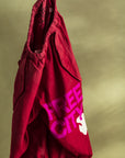 A pair of Flap/Snap LG MATTE/SATIN AirJump Pants from Free City (sparrow, LLC) is hanging against a greenish background. The pants feature the words "FREE CITY" in bold pink letters and a white dove graphic on the lower side. The waistband appears elastic, and the fabric looks casual and comfortable, boasting a custom sunfade wash for added style.