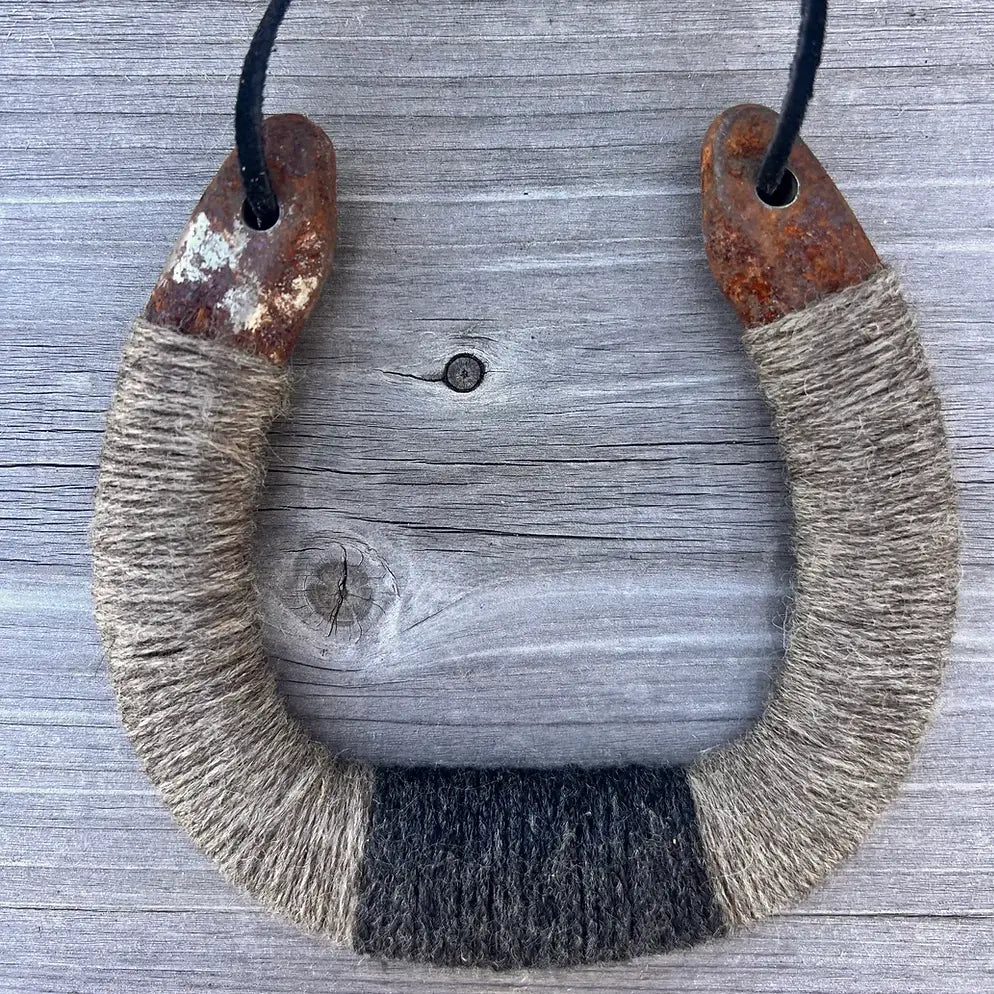 The Lucky Horseshoe by Faire features a U-shaped upcycled horseshoe with rusted ends, wrapped in coarse tan and black twine, hanging on a black cord—ideal rustic decor for your home.