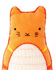 A handmade orange stuffed cat with stitched black features and a textured white tummy, crafted using the Faire Tabby Cat Embroidery Kit, is shown against a plain white background.