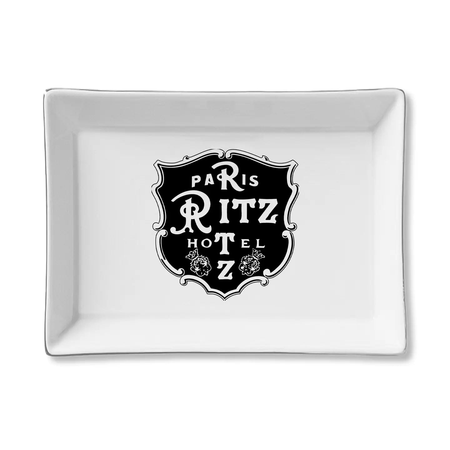 The Faire Ceramic Tray is a rectangular white ceramic piece with a black vintage-style "Paris Ritz Hotel" emblem and floral accents—ideal as a jewelry organizer or trinket tray gift.