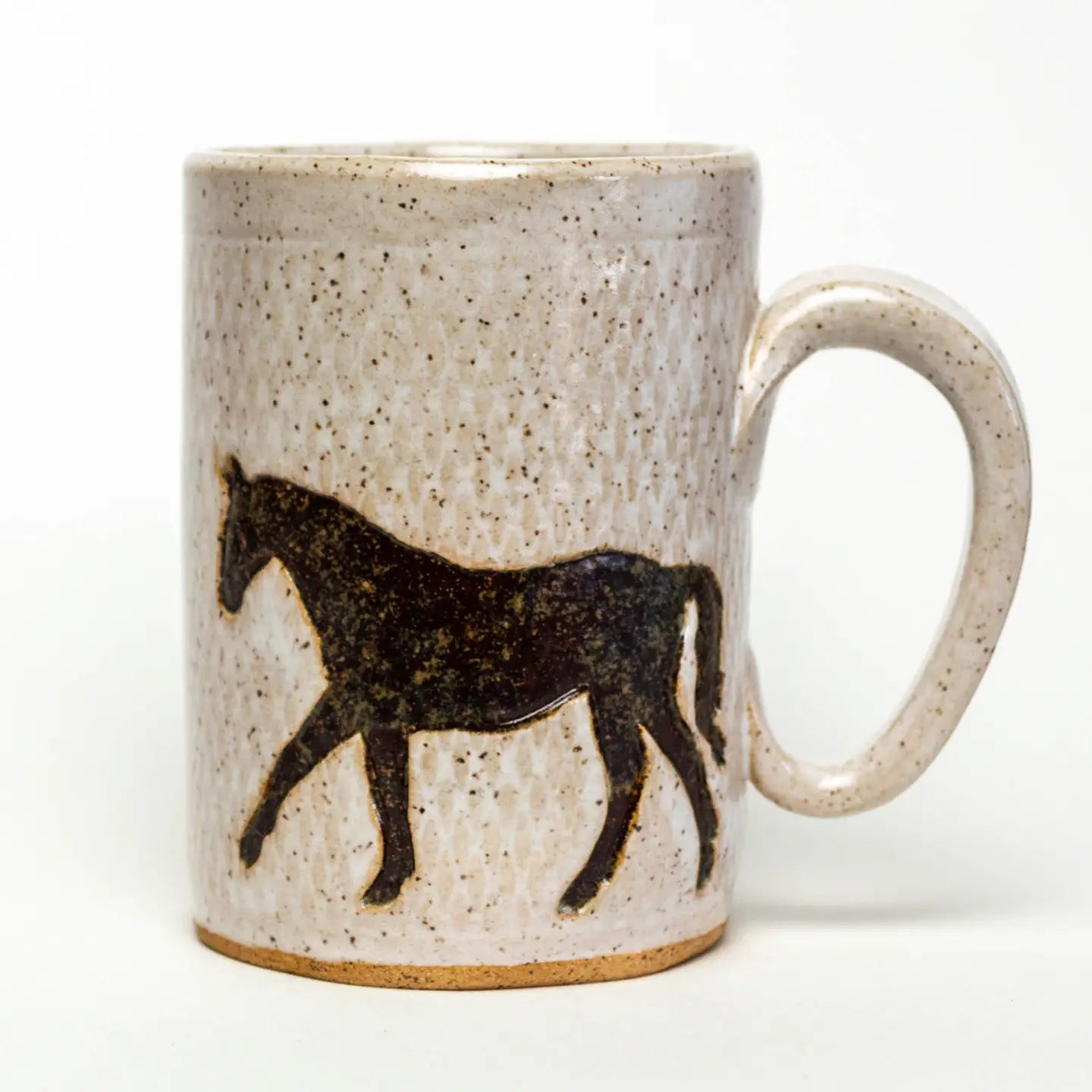 The Faire Ceramic Mug is a textured, handmade piece featuring a silhouette of a walking horse. It is dishwasher-safe with a predominantly beige color and brown speckles, while the horse design is in dark brown.