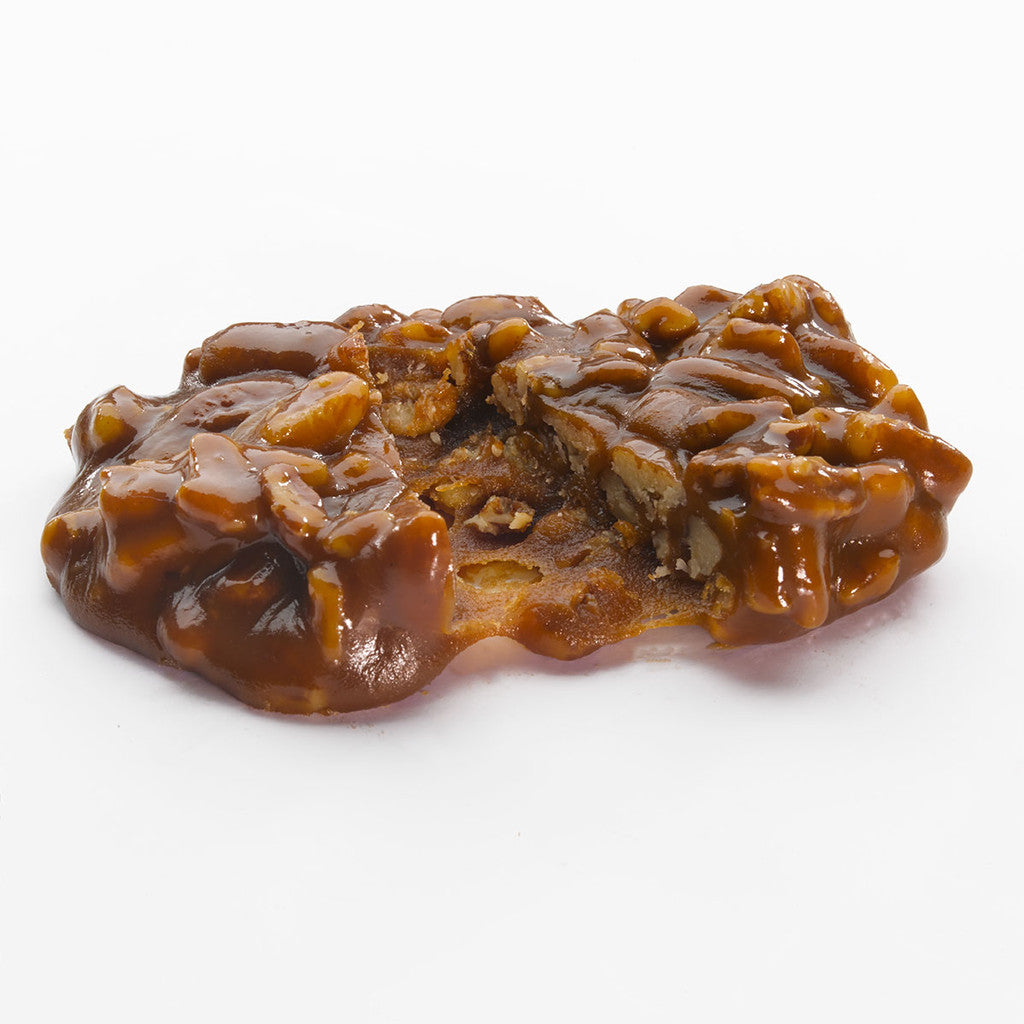 A Faire LC Pecan Pralines 1oz candy, featuring a glossy caramel coating and chopped pecans, rests on a white background with a bite taken—ideal for anyone craving pralines in bulk.