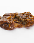 The Faire LC Texas Chewie Pecan Pralines 6oz features all-natural, chewy caramel cookies topped with whole and chopped pecans; one cookie shown with a bite taken on a white background.