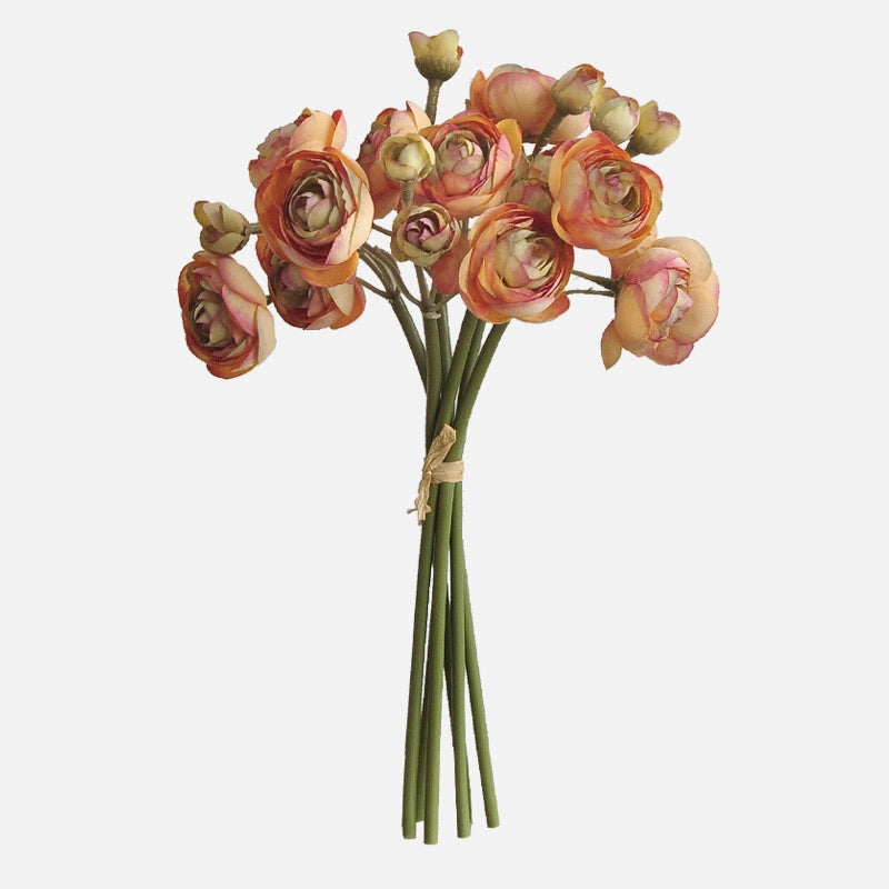 The 10'' Silk Baby Ranunculus Flower Bunch by Faire features pink and orange silk blooms, green leaves, and long stems tied with twine—perfect as multifunctional decor against a plain white background.